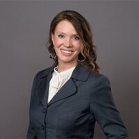 A woman in a business suit posing for a photo, featuring Caroline Beteta.