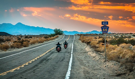 Two motorcyclists riding down an empty road at sunset.