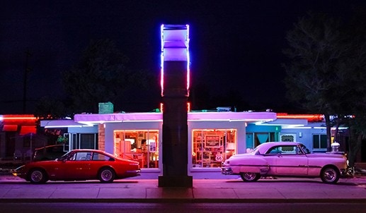 Two cars parked in front of a motel at night.