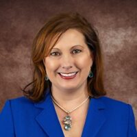 A woman, Jen Paul Schroer, in a blue suit smiling for the camera.