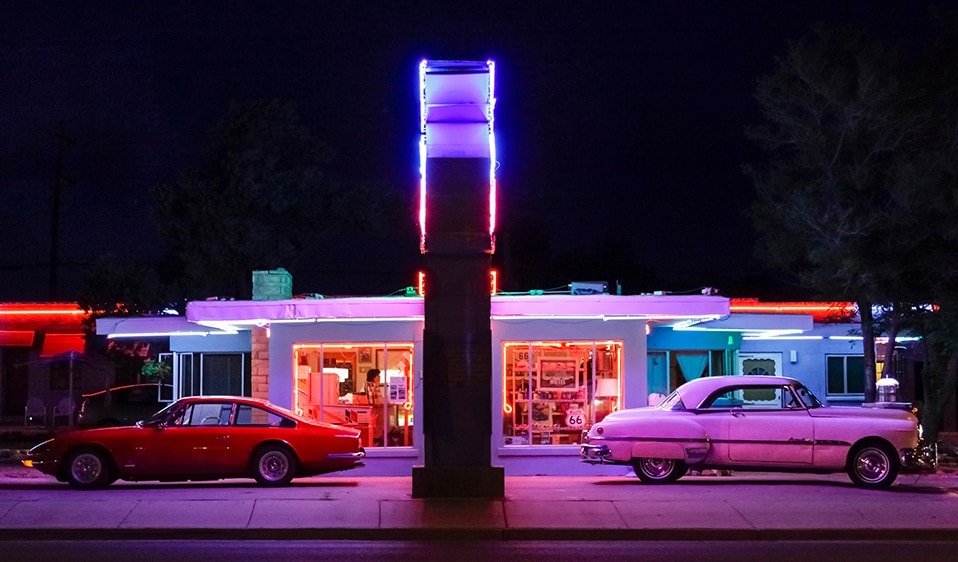 Two cars parked in front of a motel at night.