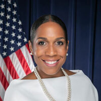 A woman wearing a white shirt and pearls in front of an American flag during an auto draft.